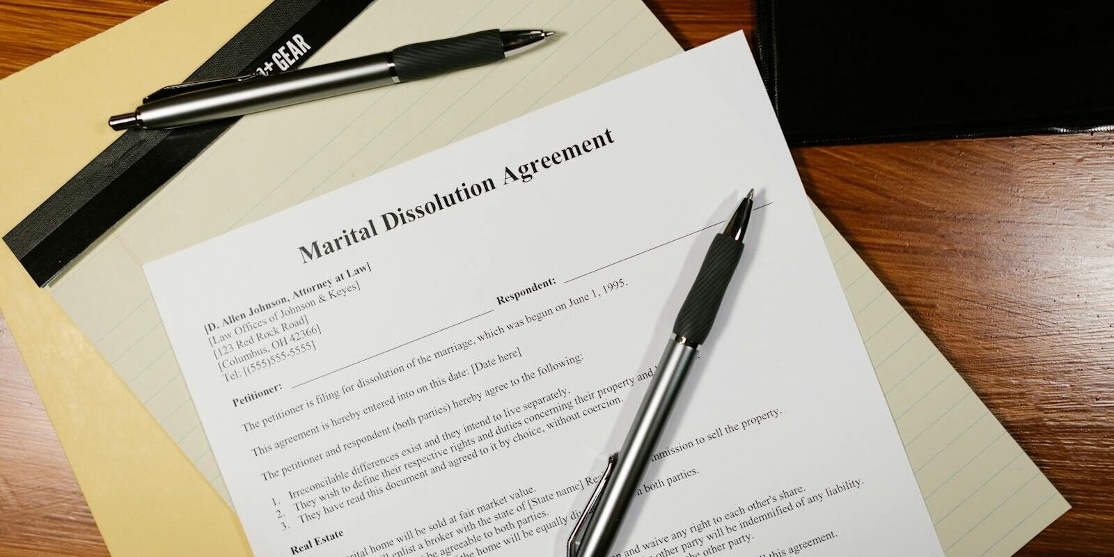 Flat lay of a marital dissolution agreement form with pens and files on a desk.